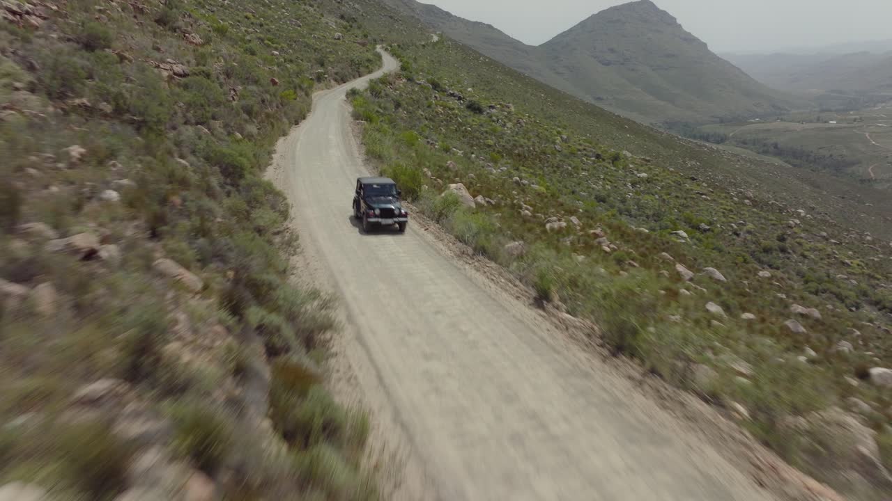 Drone flies fast over rocky landscape and road in Cederberg Wilderness Area South Africa with a view of an off-road vehicle driving on a road - you can see mountains and the tail