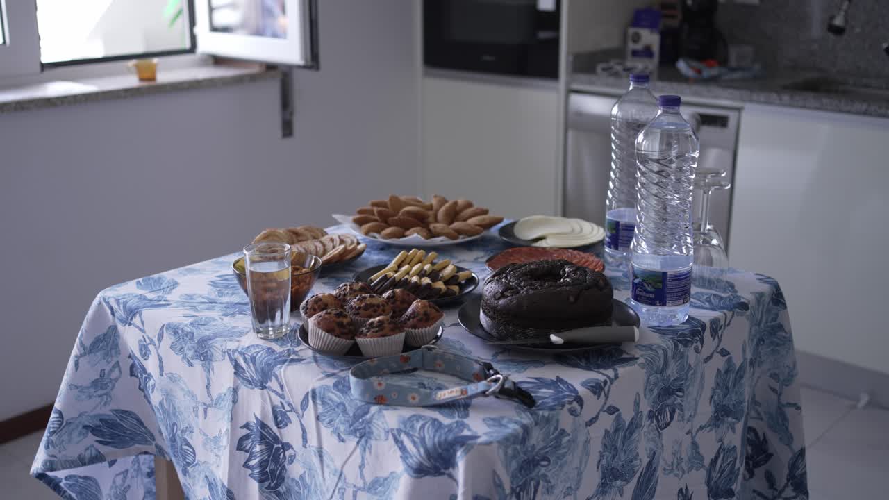 Variedad de pasteles, bollería y snacks caseros dispuestos sobre una mesa de cocina con botellas de agua