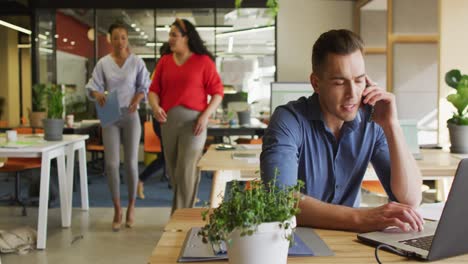 Happy-caucasian-businessman-sitting-at-table-and-using-smartphone-at-office