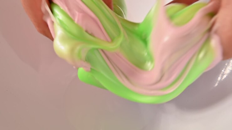 Woman mixing green and pink slime on a white background