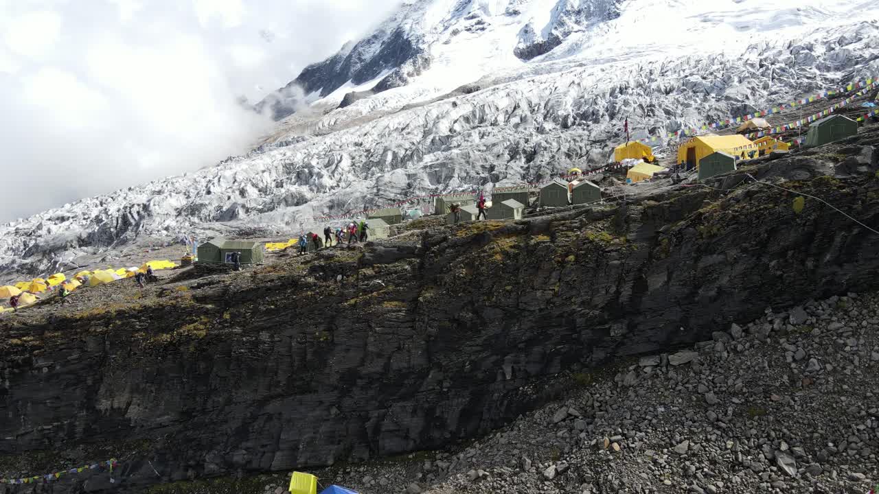 Drone footage showcases Manaslu Base Camp below the 8,163m Himalayan peak. The scene reveals snowy ridges, rugged terrain, and the dramatic high-altitude environment of this remote mountain region