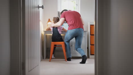 view through bedroom door as father helps daughter using laptop on desk