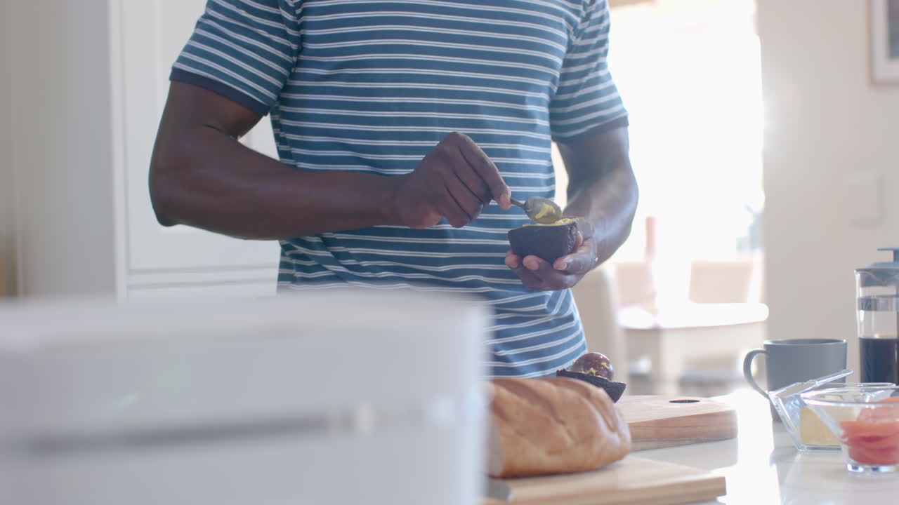 African american man preparing avocado toasts in sunny kitchen, slow motion