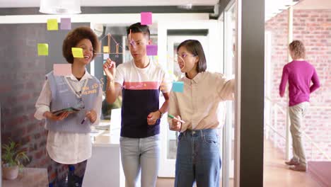 Three-diverse-male-and-female-creative-colleagues-brainstorming-ideas-on-glass-wall,-slow-motion