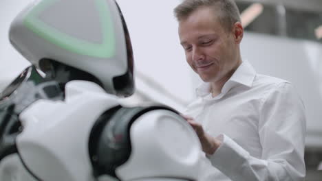 a man stands with a robot bot and asks him questions and asks for help by clicking on the screen on the robot body. human-robot interaction in the modern world