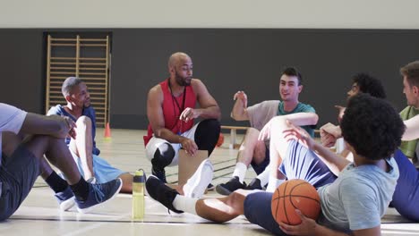 happy diverse male basketball team training with male coach in indoor court, in slow motion