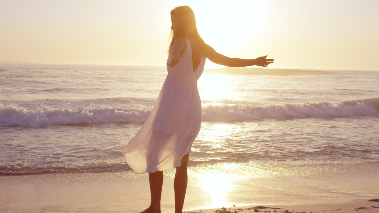 자유로운 행복한 여성 팔을 펴고 자연을 즐기며 해가 지는 해변에서 춤을 추고 느린 움직임의 빨간 용