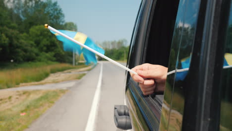 Hand-Mit-Schweden-Flagge-In-Einem-Autofenster-Reise-Skandinavien-Konzept