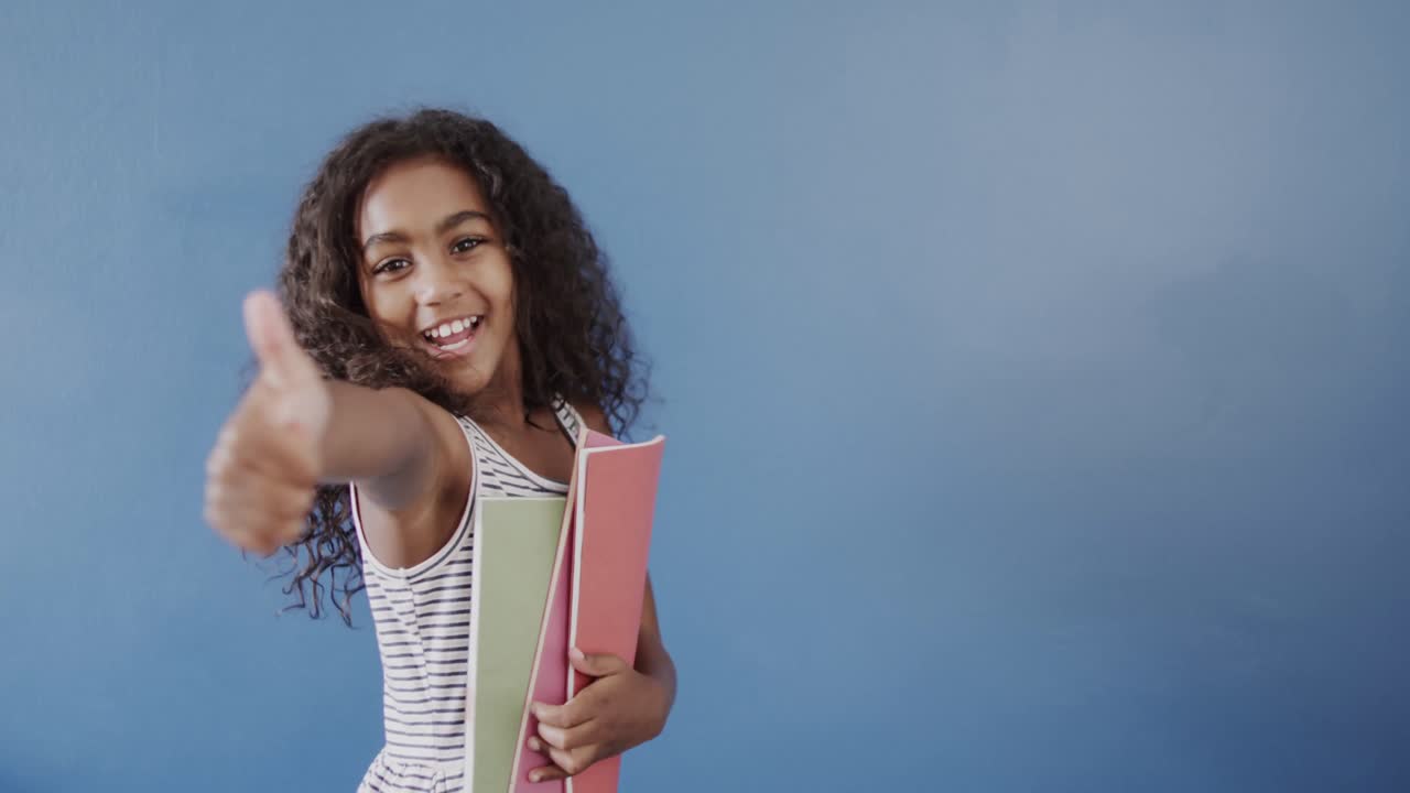 retrato de una feliz chica afroamericana sosteniendo libros en un fondo azul, espacio de copia, cámara lenta