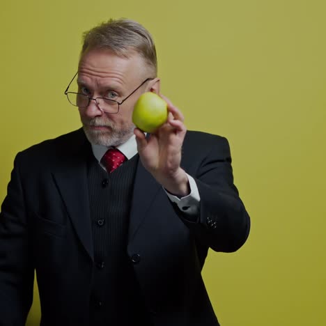 smiling senior businessman with fresh fruit. happy elderly man in elegant suit tries to eat apple and looking at camera. positive emotions.