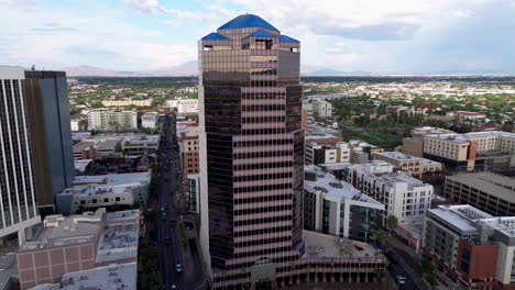 A-4k,-wide-aerial-shot-flying-up-while-panning-down-on-a-building-in-downtown-Tucson,-AZ-with-the-mountains-in-the-background-and-the-city-surrounding