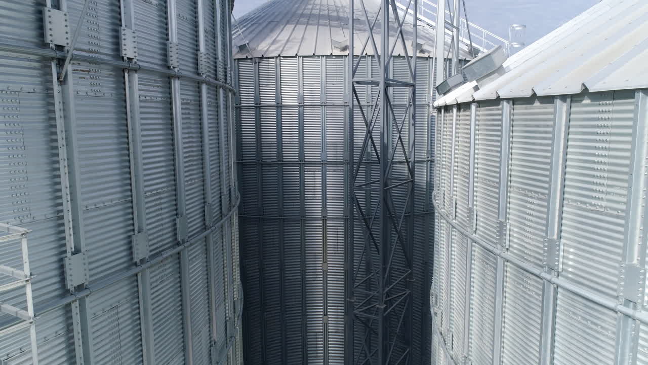 Exterior of large metal granaries. Silver elevators for keeping crop. Modern hangar premises. Agriculture storage tanks. View from drone.