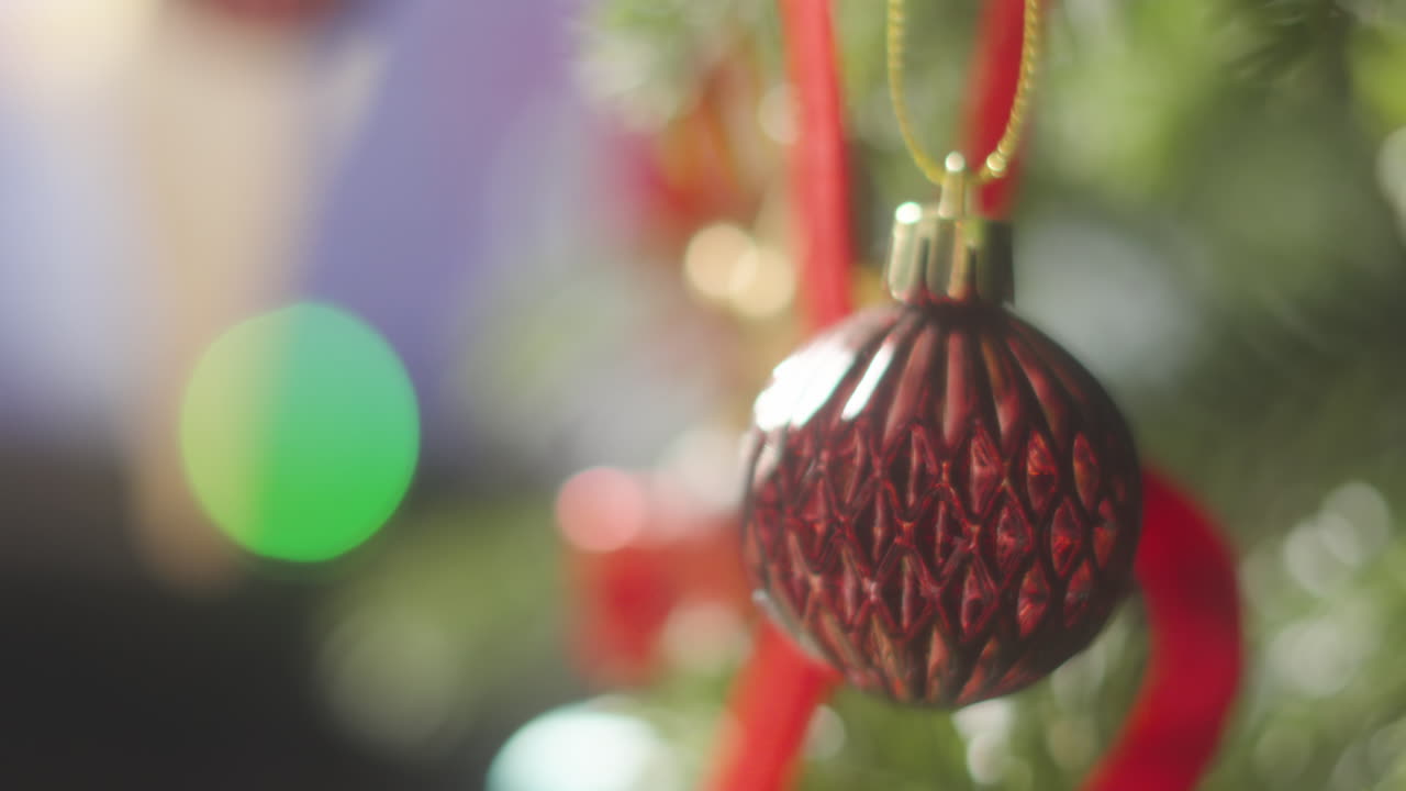 Decorative Style Red Christmas Bauble Hanging on Xmas Tree with Bokeh Lights in Background with Sun Haze Lighting in Cozy Home Environment. Happy Merry Festive Seasonal Decoration