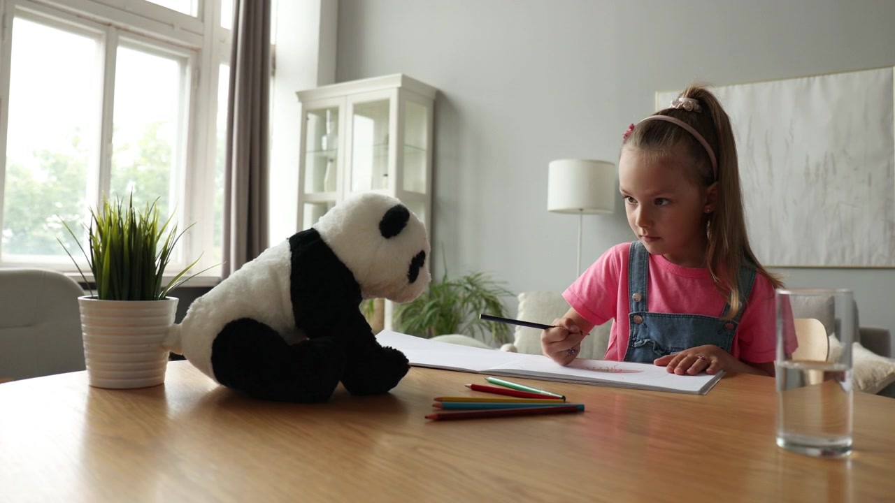 Little Girl Drawing in Notebook with Panda Toy