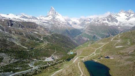 aerial view of zermatt, showcasing the iconic matterhorn mountain surrounded by snow-capped peaks, lush green valleys, winding roads, and a serene alpine lake in the foreground