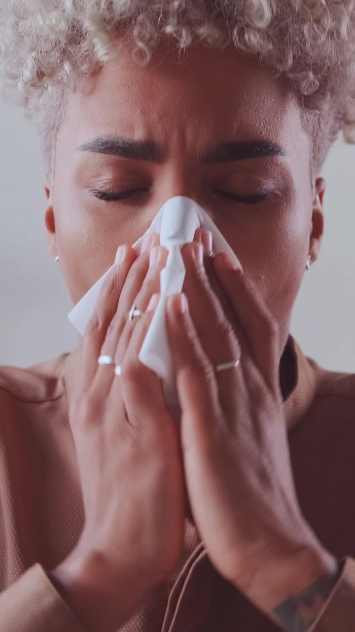 Sick african american woman sneezing into tissue and blowing her nose