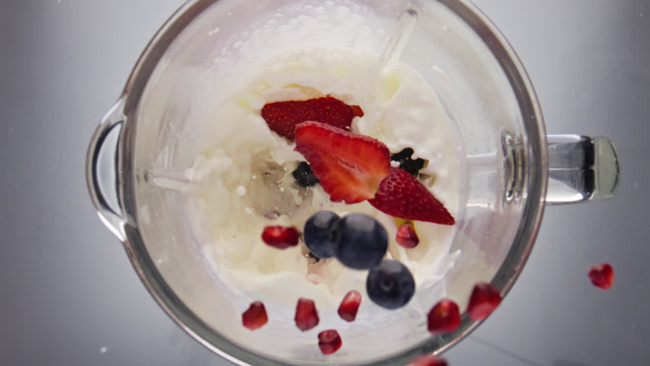 Milkshake fragola e mirtillo che cade e si frulla con il mixer, primo piano, vista dall'alto.