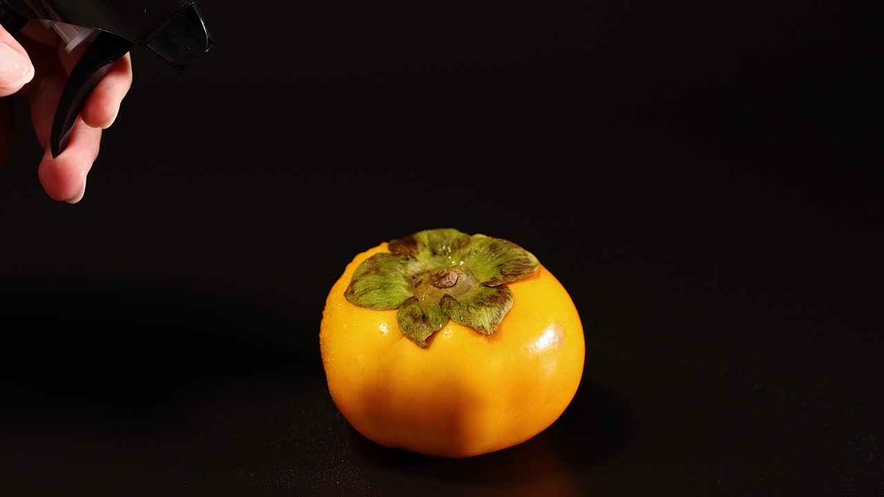 la mano rocia agua en una fruta de caqui
