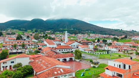 misty mountains tower behind guatavita’s charming red-roofed town in this stunning pedestal shot