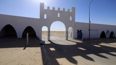 la antigua puerta del sáhara iluminada por el sol con cielo azul, arena en el suelo, graffiti en las paredes, patrones de sombras