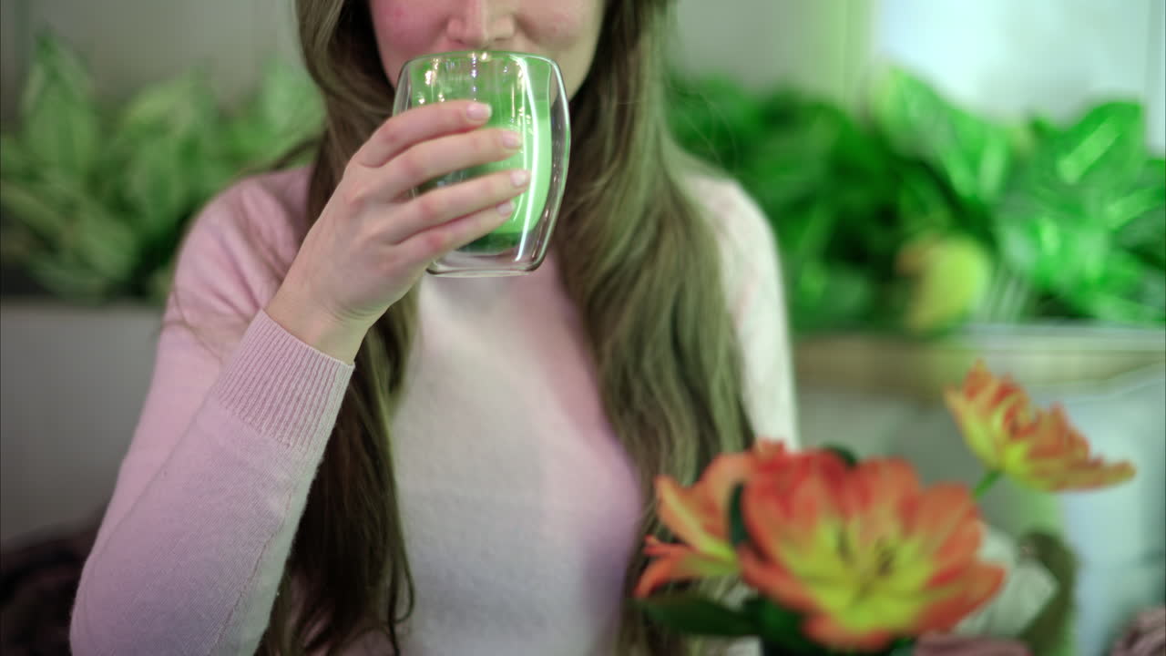 Woman in eco friendly restaurant drinking matcha. Flowers in foreground