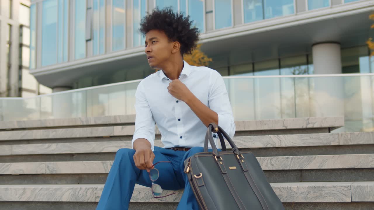 Upset african american businessman sitting on stairs outdoors business center