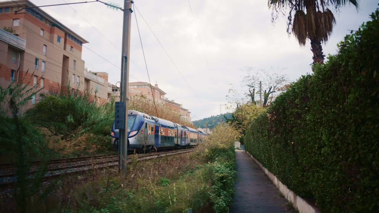 Golfe Juan, France - November 26, 2025: A fast moving double decker train rushes past railway tracks surrounded by wild vegetation