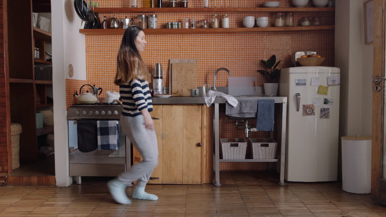donna asiatica felice che balla in cucina celebrando uno stile di vita di successo godendo di una allegra celebrazione della danza della vittoria a casa nel fine settimana