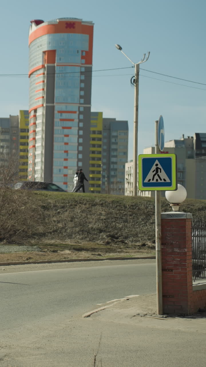 vista cercana de un paisaje urbano con una señal de cruce de peatones, un coche girando en la carretera y edificios de gran altura en el fondo, con dos personas caminando juntas