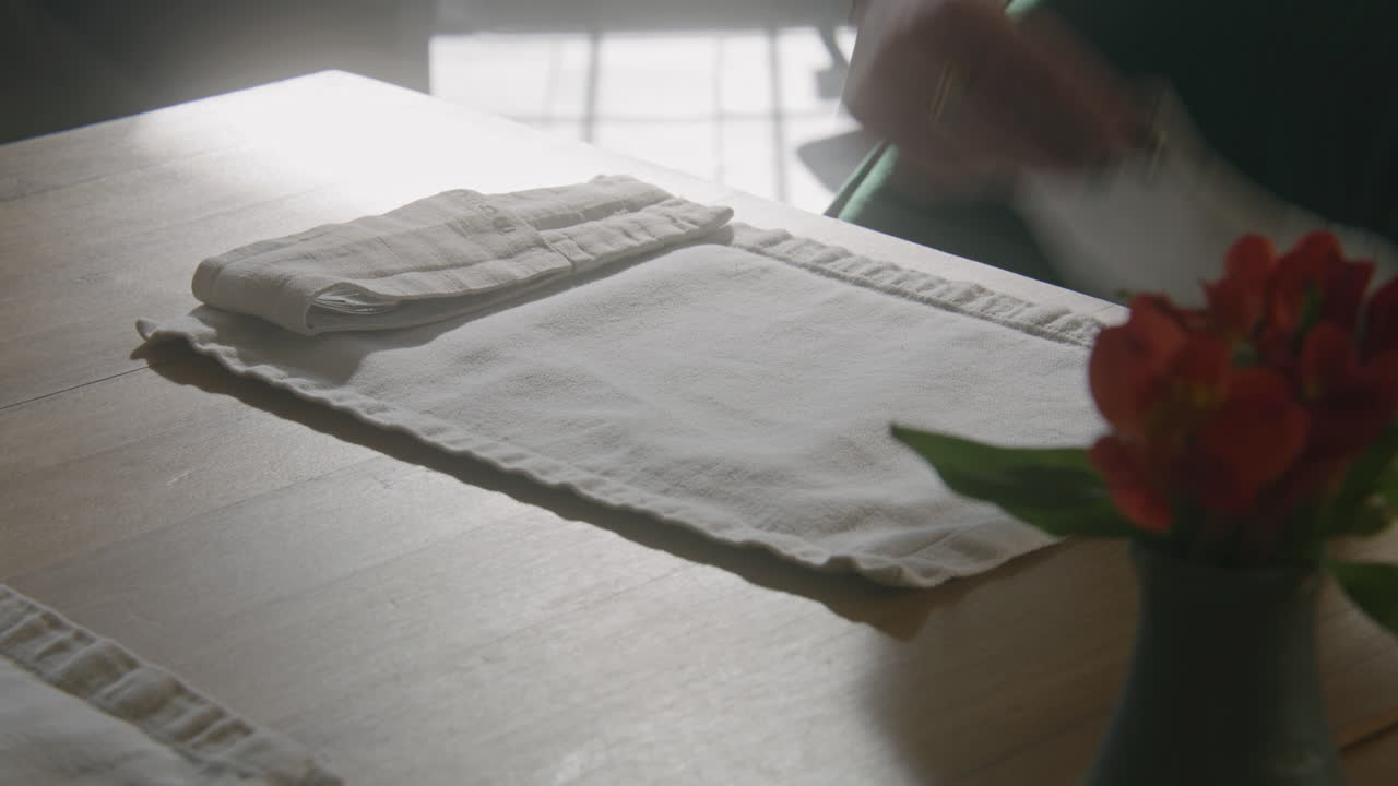 Table setting with flowers and hand placing placemat