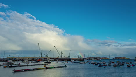 zeitraffer von booten, die tagsüber einen industriellen schifffahrtshafen segeln, während der regenbogen in den wolken erscheint