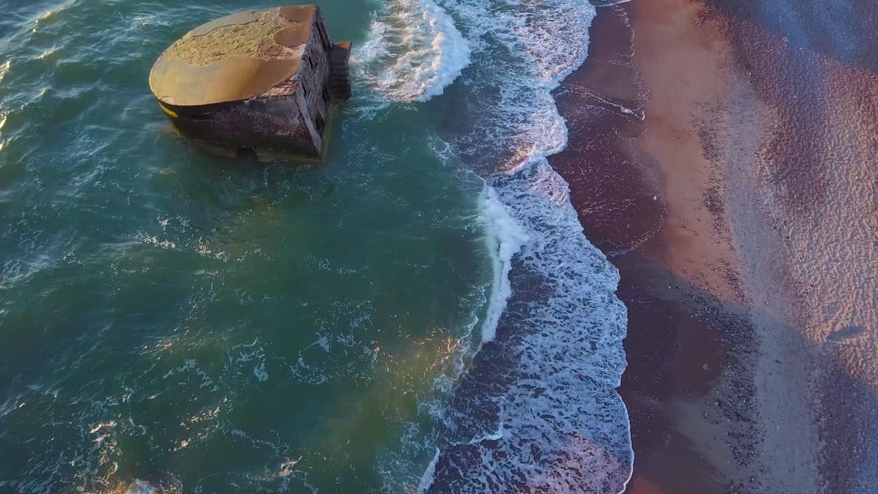 vista aérea de los edificios de fortificación costeros abandonados en los fuertes del norte de karosta en la playa del mar báltico, salpicaduras de olas, puesta de sol de la hora dorada, disparo de drones avanzando