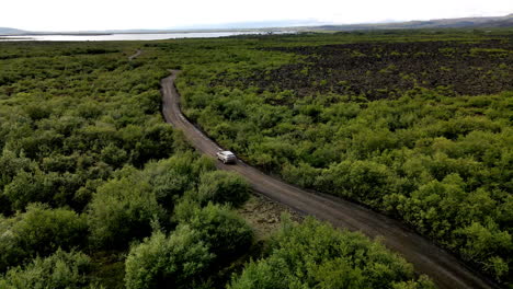 aerial tracking shot of a car following the gravel road in between the green trees in iceland