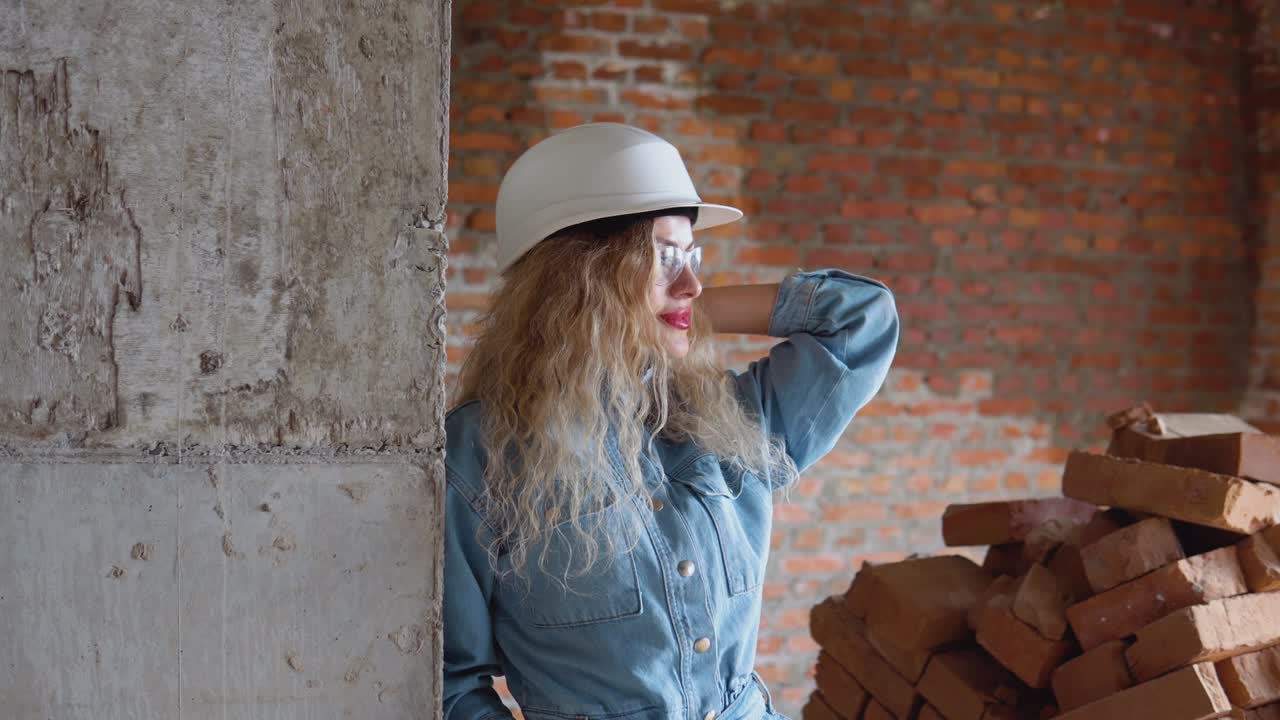 Una giovane donna con un casco da lavoro, vestiti di jeans e occhiali protettivi si trova in cantiere. Estetica delle professioni lavorative.