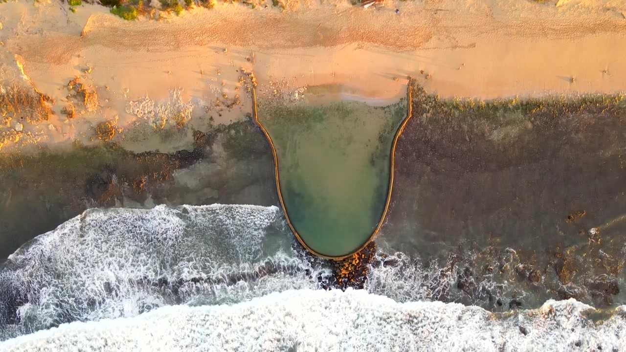 Witsand marine tide pool juts out from sandy beach into ocean, top down aerial