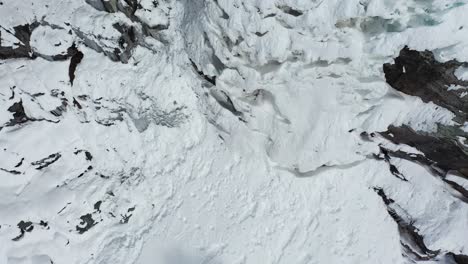 Frozen-Waterfall-in-Cold-Winter-Mountain-Landscape-Birdseye-Dramatic-Aerial-View-From-Top-to-Foot-of-Fall,-Drone-Shot