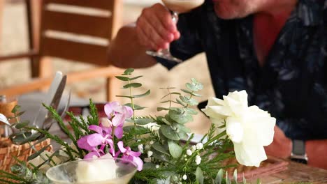 a person sips a cocktail surrounded by vibrant tropical flowers. warm lighting and a relaxed atmosphere enhance the scene