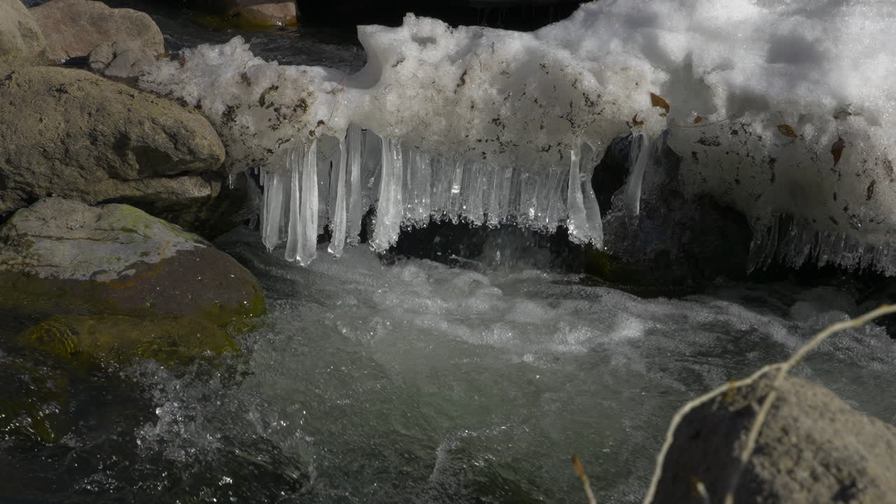 Icicles And Snow Melting In The Rocky River During Winter. - zoom in shot