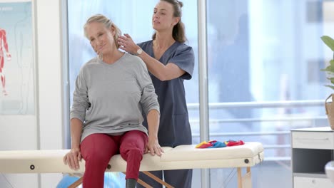 caucasian female physiotherapist stretching neck of female senior patient at rehab center