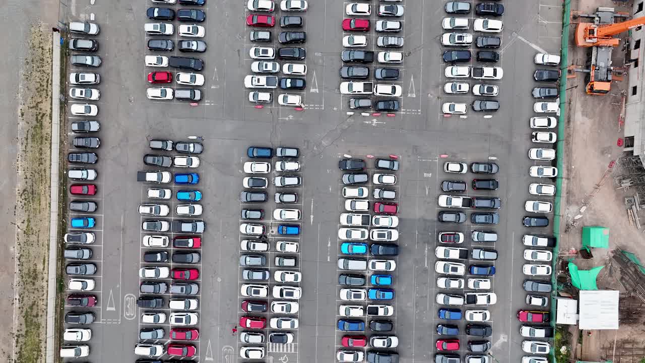 Top-down drone aerial of full parking lot with organized rows of colorful cars in geometric patterns, construction tents visible