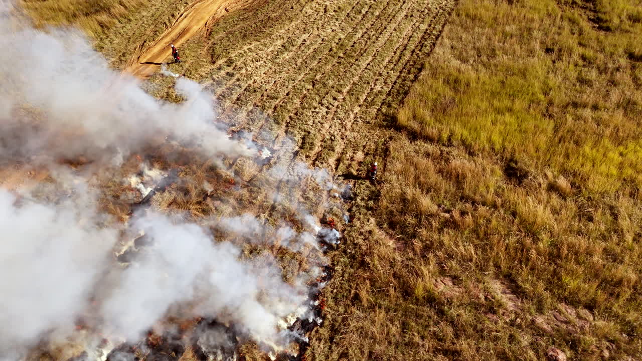 Planned burn in rural farm field with workers on the fire line, aerial tilt-up