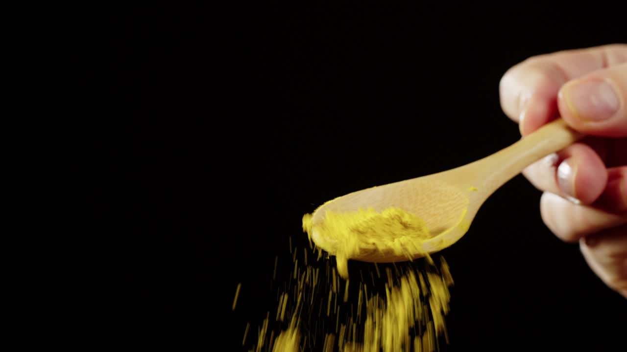 Hand Sprinkling Yellow Turmeric Powder from Wooden Spoon