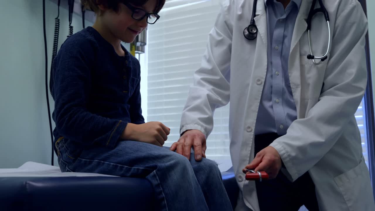 Front view of young asian male doctor examining caucasian boy patient knee in a clinic 4k