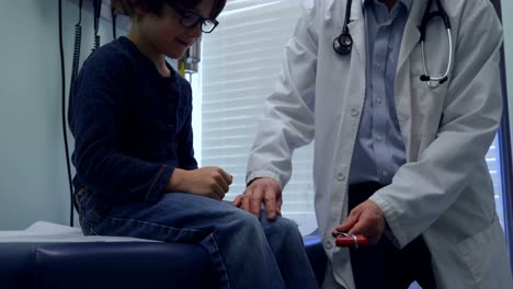 vista frontal de un joven médico asiático examinando la rodilla de un paciente caucásico en una clínica 4k