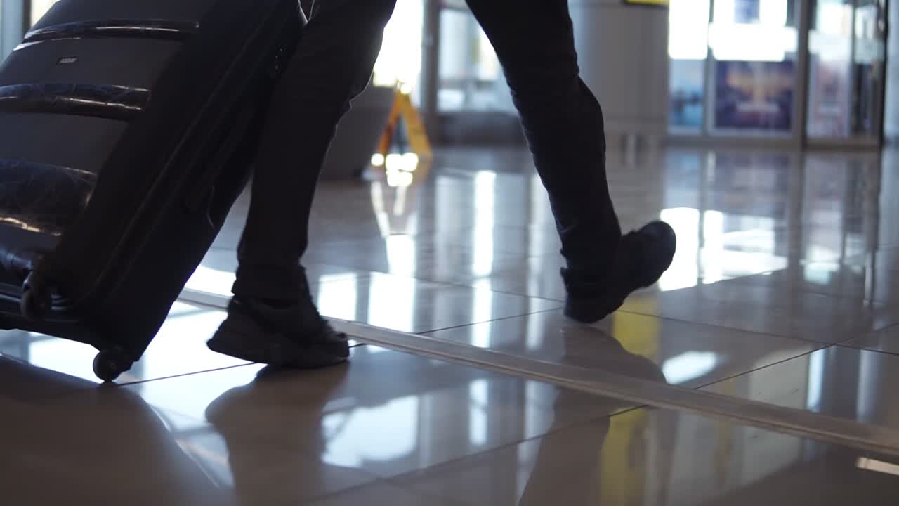 Close up, cropped shot of man legs with the black baggage walking to the airport terminal. Slow motion