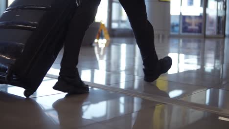 Close-up,-cropped-shot-of-man-legs-with-the-black-baggage-walking-to-the-airport-terminal.-Slow-motion