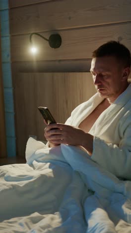 Relaxing evening routine in cozy bedroom with a man using his smartphone while in bathrobe