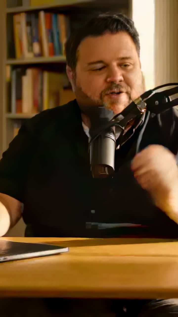 Vertical video: Leaning man in dark shirt speaking into mic at home studio, recording on laptop