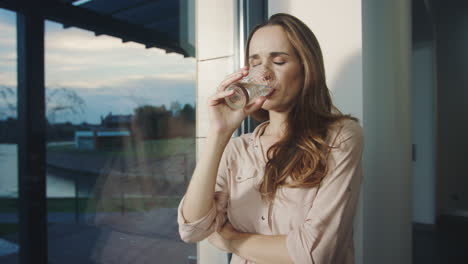 Mujer-Relajada-Bebiendo-Agua-Cerca-De-La-Ventana-Panorámica.-Señora-Sedienta-Bebiendo-Agua