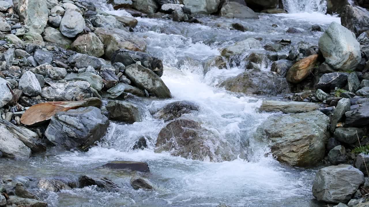 Clear mountain stream rapidly flows over large rocks and boulders in a natural outdoor setting. Static camera, natural daylight, crisp detail